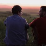 two men sitting and talking at sunset