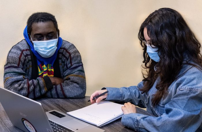 A peer counselor sits at a table talking to a client about their care.