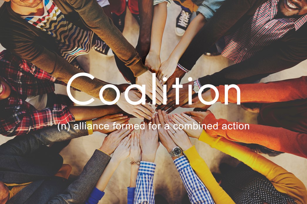Photo of a circle of people all holding their hands in a pile in the center with overlayed text reading "Coalition: (n) alliance formed for a combined action"