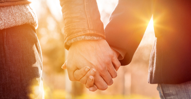 Hands of two people clasped in front of a rising or setting sun