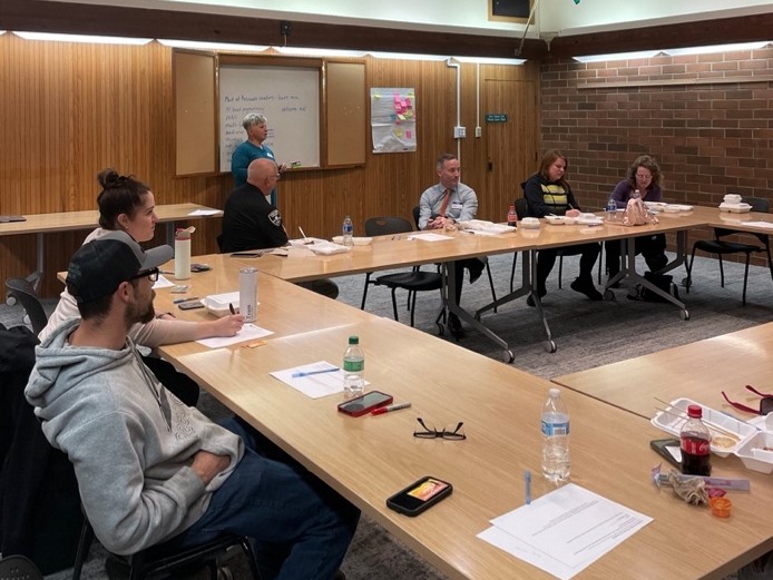 People sitting at meeting tables with a speaker in front writing on a board