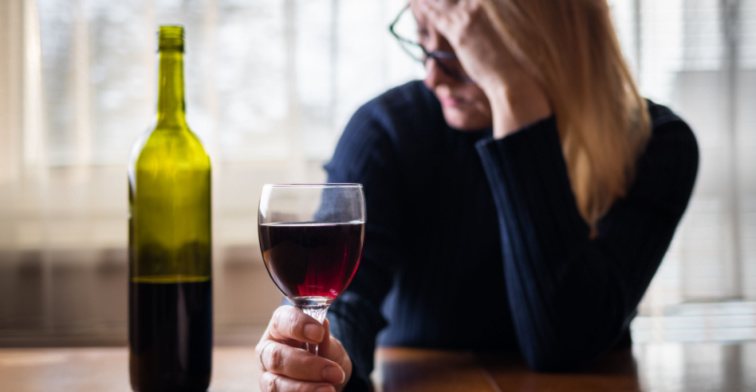 Woman holding glass of wine with one head and resting forehead in other hand